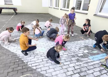 Uczniowie 1b malują serce na dziedzińcu szkolnym.