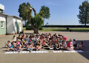 Uczestnicy akcji podczas czytania książek na szkolnym dziedzińcu